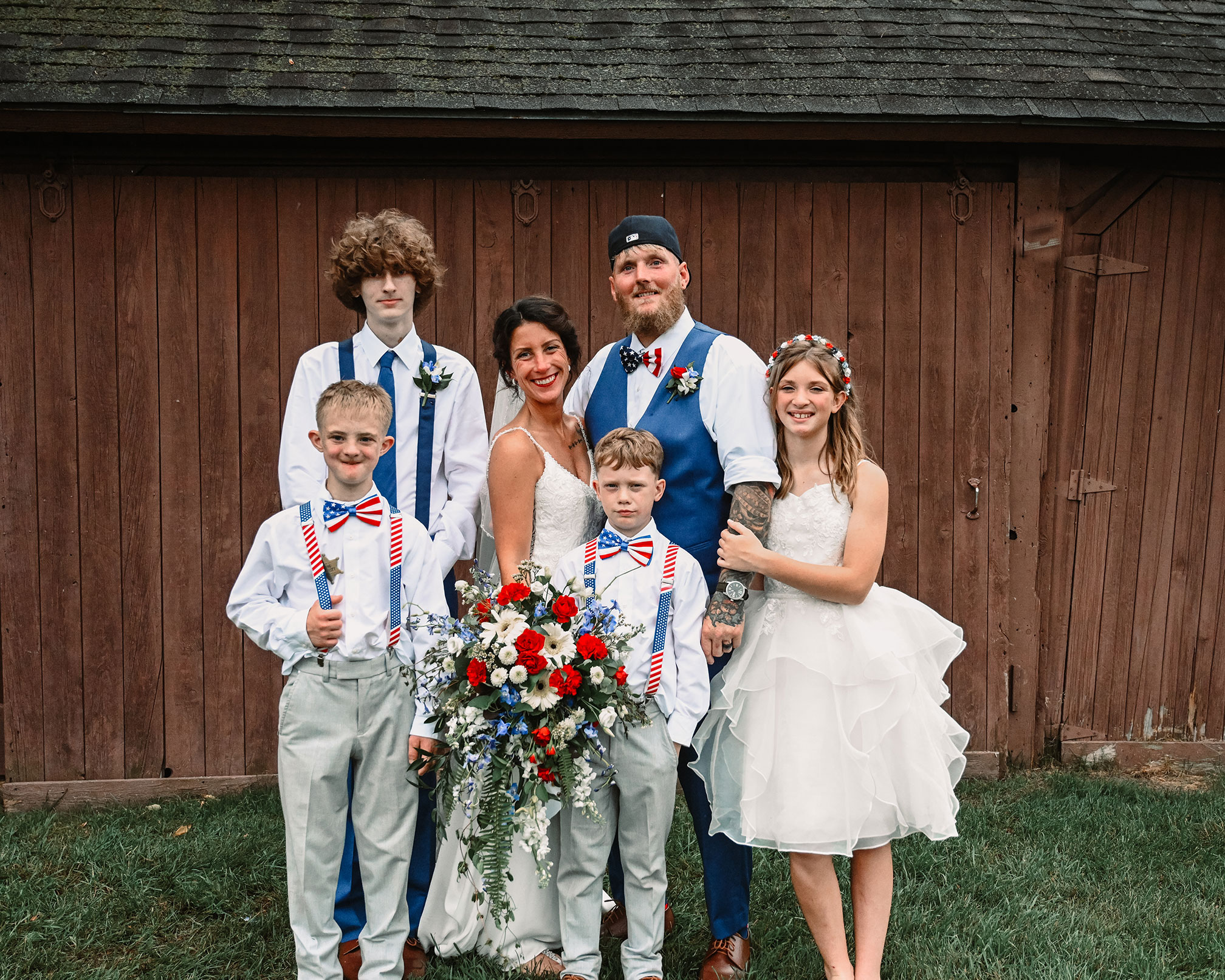Bride and groom, Erica and Charlie, stand together on their wedding day, smiling with their four children gathered around them, forming the close-knit core family behind New Creations Construction.