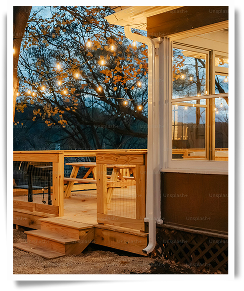 Outdoor living space featuring a deck in early spring connected to a three-season room, softly lit with string lights to create a cozy setting for both private relaxation and social gatherings while enjoying the outdoors.